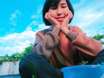 Low angle view of smiling young woman sitting against sky