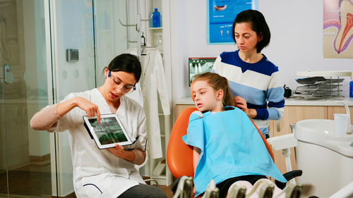 Dentist showing medical report to girl and her mother at clinic