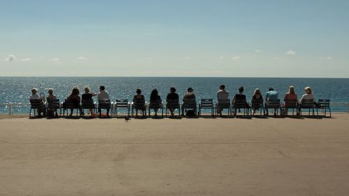 Rear view of people sitting on chair against sea