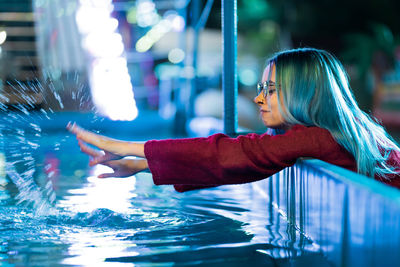 Side view of young woman splashing water in pool