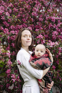 Smiling woman with baby boy standing in front of apple blossom tree