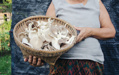 Midsection of woman holding mushrooms in basket