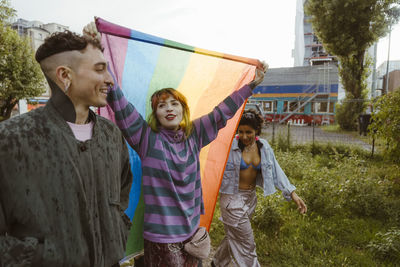 Woman holding lgbt flag while walking with non-binary friends at park