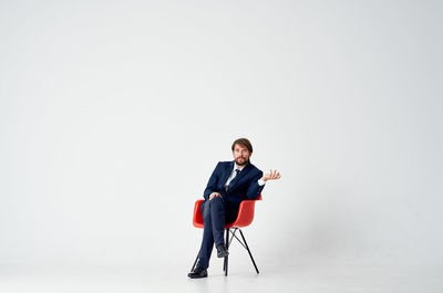 Young man sitting on chair against white background