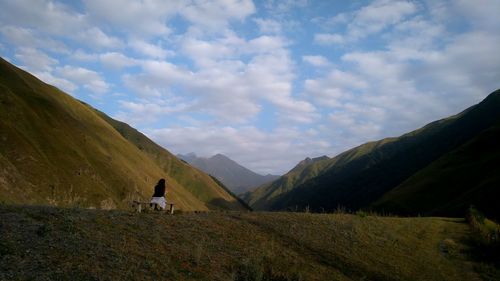 Woman sitting on bench against mountains