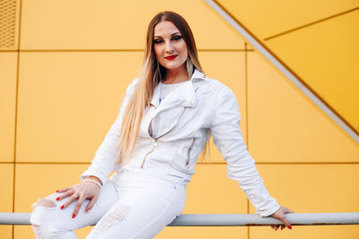 Portrait of young woman sitting on railing against wall