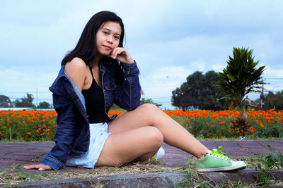 Portrait of young woman sitting on plant against sky