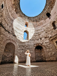 Woman standing inside ancient roman building with natural light shining on her.