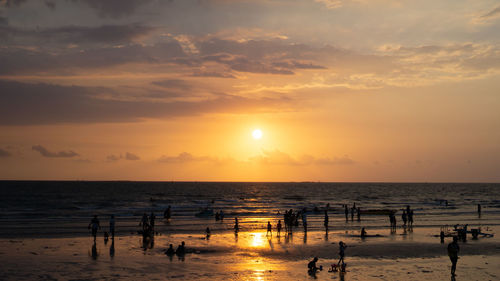 Silhouette people on beach against sky during sunset