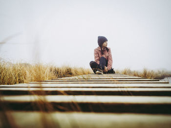 Woman looking away while sitting on footbridge against sky