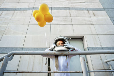 Girl leaning on railing while holding yellow balloon
