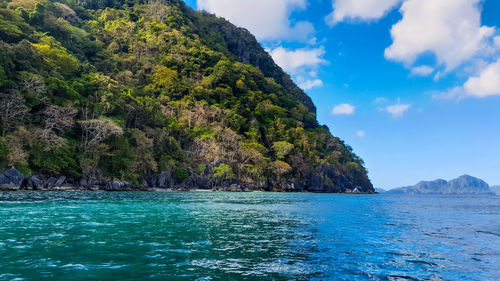 Scenic view of sea by mountain against sky