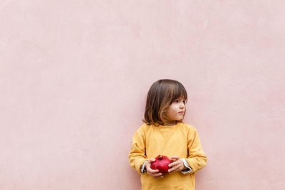 Little girl with blond hair holding red pomegranate in her arms