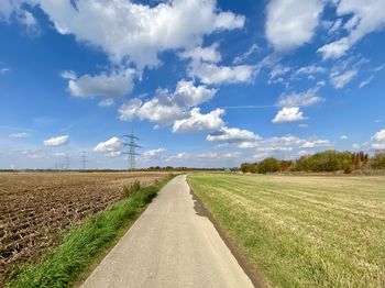 Empty road amidst field against sky