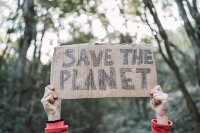 Cropped unrecognizable ethnic child showing save the planet title on carton piece while looking at camera in forest