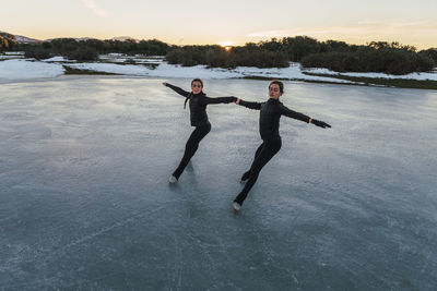 Two female figure skaters practicing together on frozen lake at dusk