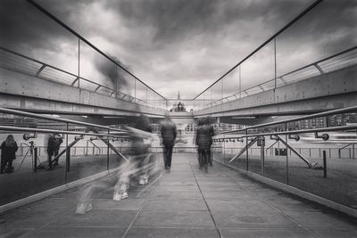 Blurred image of people walking on millennium bridge against cloudy sky