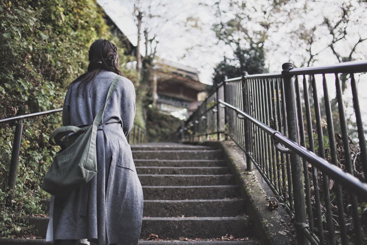 railing, real people, rear view, architecture, lifestyles, day, one person, plant, tree, built structure, standing, leisure activity, nature, staircase, bridge, three quarter length, connection, focus on foreground, the way forward, footbridge, bridge - man made structure, outdoors, warm clothing