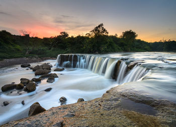 Scenic view of waterfall against sky during sunset