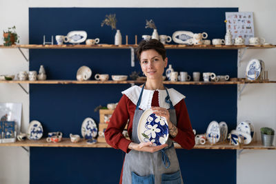 Craftswoman posing with handmade plate after decorating pottery with hand drawn ornament