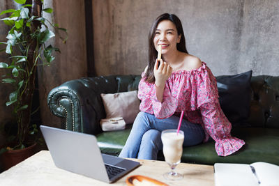 Smiling young woman using phone while sitting on sofa