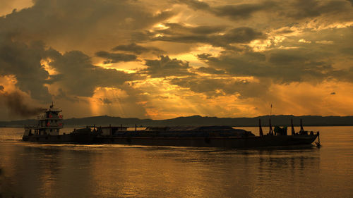 Silhouette boat sailing in sea against sky during sunset