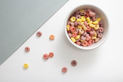 Breakfast cereal concept, colorful ring cereals in bowl and falling on grey and white background.