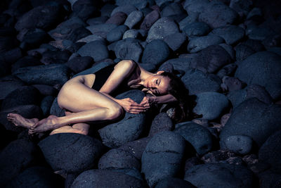 Female model in swimsuit lying on rocks at beach