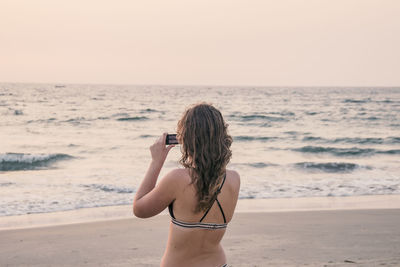 Rear view of woman photographing sea against clear sky