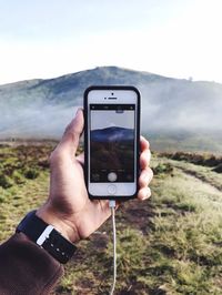 Close-up of man hand photographing mountain with smart phone