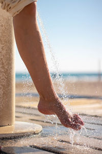 Woman wetting her feet with a shower to clean them from the sand after leaving the beach.