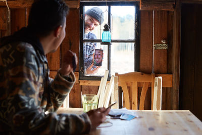 Man showing photograph over smart phone to friend sitting in cottage