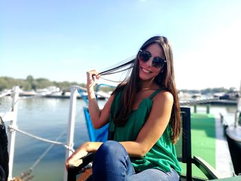 Portrait of smiling young woman sitting on boat in river against sky