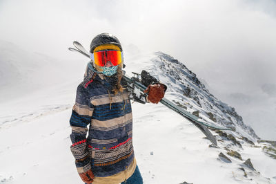 Portrait of a pretty and active woman skier, wearing a mask and holding skis in her hands, active