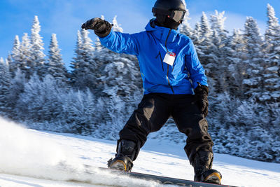 Man snowboarding on snowy land against trees