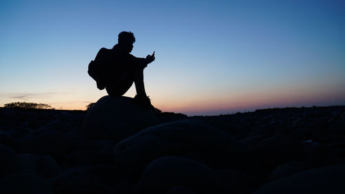 Silhouette man on rock against sky during sunset