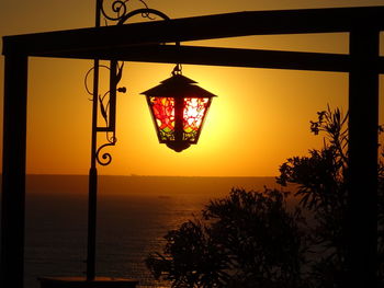 Illuminated lamp post by sea against sky during sunset