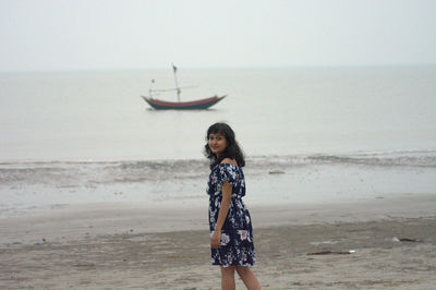 Young woman standing at beach against sky