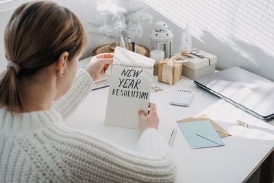 2022 goals, new year resolution. woman in white sweater writing text new year resolution in open