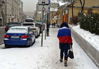 Rear view of woman walking on snow covered city