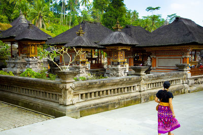 Rear view of woman walking towards temple against trees