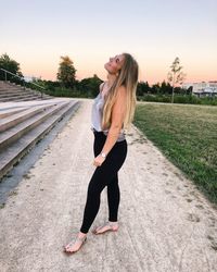 Full length of young woman standing on road against sky