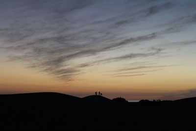 Silhouette friends on sand dune against sky during sunset