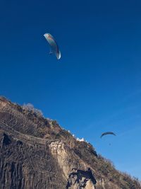 Low angle view of person paragliding against blue sky