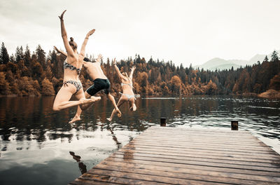 People jumping by lake against sky