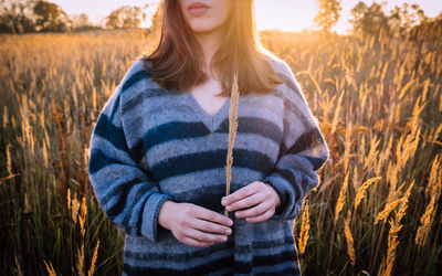 Midsection of woman holding crop against agricultural field