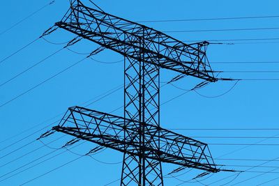 Low angle view of electricity pylon against blue sky