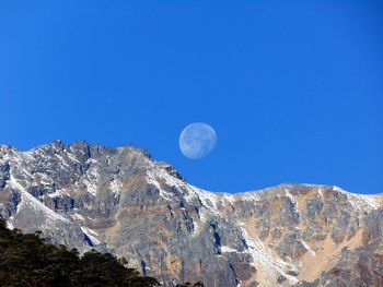 Low angle view of snowcapped mountains against clear blue sky