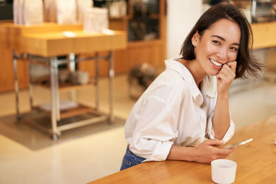 Portrait of young woman using mobile phone while sitting on table