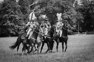 Men riding horses on field against trees